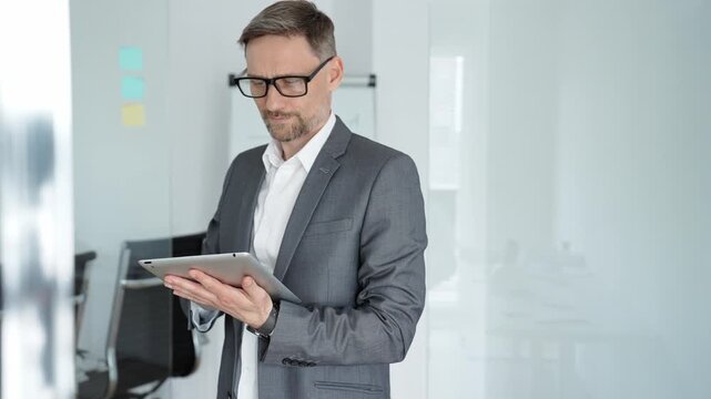 Businessman using a digital tablet while reviewing and arranging adhesive notes on a glass wall, strategizing and planning a project in a corporate environment
