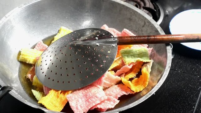 Close-up of frying colorful Indonesian crackers in hot oil. Traditional snack preparation featuring vibrant crackers, authentic local cuisine, homemade cooking, crispy texture, and delicious street fo