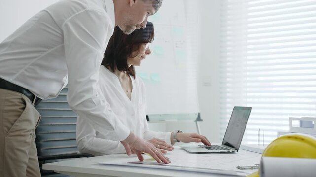 Architects collaborating on building design, reviewing blueprint plans and architectural models, creating detailed floor layout sketches in a professional office environment
