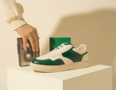 Hand reaching for wallet near sneaker on pedestal in modern setting with green accents and neutral colors from a frontal viewpoint in a product photo