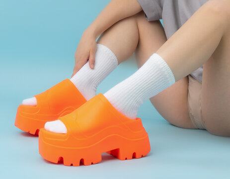 Close-up View of Person's Feet in Vibrant Orange Shoes with White Accents on Bent Knees in Gradient Environment
