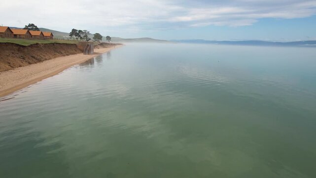 A flight over the shore of Lake Baikal on a summer day. The water is calm, a beautiful turquoise color.