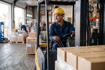 Fototapeta premium Warehouse worker driving forklift with cardboard boxes