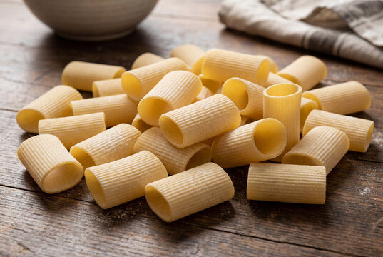 Pile of raw uncooked paccheri pasta tubes resting on a rustic dark wooden kitchen table