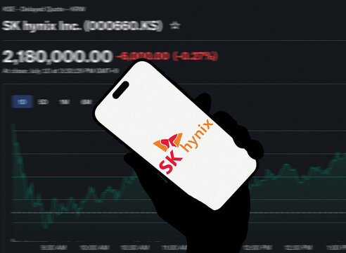 SK Hynix Logo Displayed on Smartphone Screen Held in Silhouette Hand Against KOSPI Stock Price Chart Background