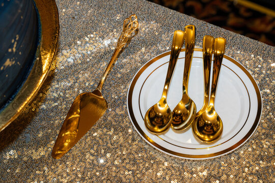 elegant gold cake server and dessert spoons arranged on a white plate with gold trim, displayed on a sparkling sequined tablecloth for a formal celebration
