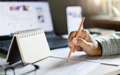 Fototapeta premium close up shot, man hand holding pencil checking document, business contract and making note in calendar pad working with laptop start online business, e-commerce