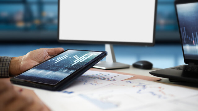 close-up shot, man hand using digital tablet analyzing chart make investment plan and working on table with computer
