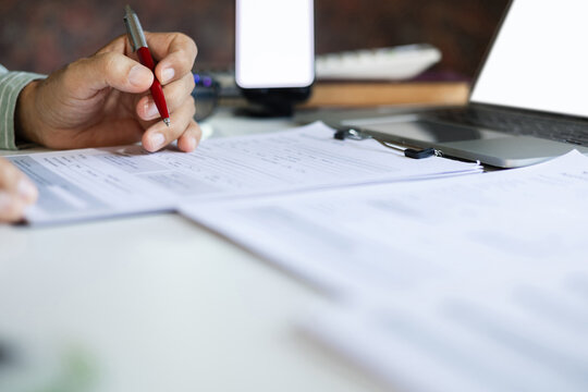 close-up shot, man hand reviewing business contract and verify the accuracy of the document and using laptop work on desk