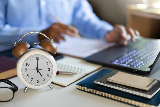 close up shot alarm clock 5 PM in front and blurred  businessman using laptop work in office and start over time work