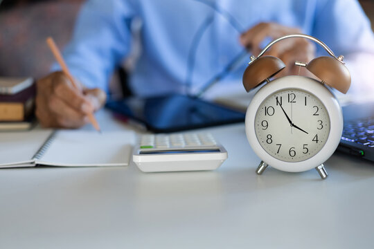 close up shot alarm clock 4 PM in front and blurred  businessman working in office hurry up and get the work done before end of work time at 5 PM