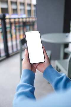 Vertical mockup image of a woman holding and using mobile phone with blank desktop screen in cafe