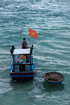 Minimalist seascape of a small fishing boat towing a coracle off Ly Son Island with a fisherman on bow and Vietnamese flag flying