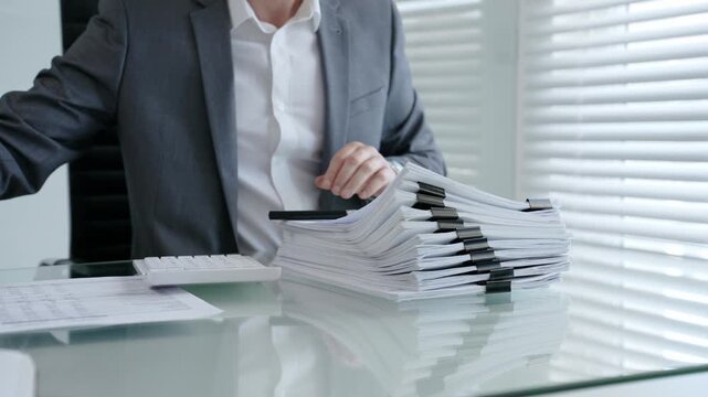 Business professional meticulously inspecting a contract or official document with a magnifying glass and pen while working at a desk with a stack of paperwork