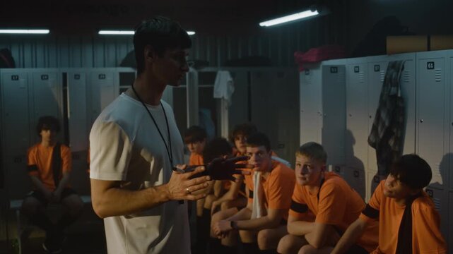 Passionate Male Coach Stands Before Diverse Group of Teenage Football Players in Locker Room. Man Gestures, Giving Motivational Pre Match Instructions and Tactical Advice. Sports Mentorship, Strategy.