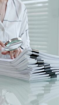 Woman's hands using a magnifying glass to scrutinize a document while holding a pen, researching important information for legal, financial, or academic analysis and validation