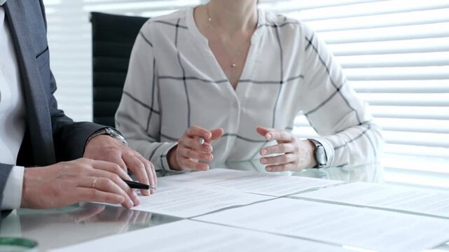 Business professionals discussing a contract, agreement, or important partnership documents during a meeting in an office setting, signing paperwork for a deal