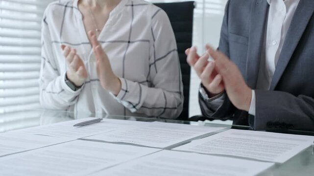 Business professional hands clapping in appreciation or congratulating an achievement. With important legal documents and a pen on a glass table. Symbolizing successful negotiations and a signed deal.