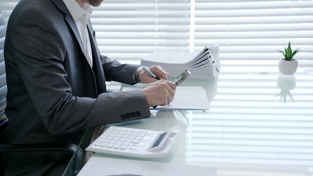 Businessman using a magnifying glass to meticulously examine a financial document at a modern office desk, scrutinizing details for accuracy and compliance in auditing processes