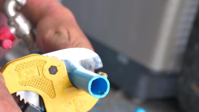 Close-up of a person cutting a PVC pipe with a pipe cutter during a DIY home plumbing repair, preparing plastic pipe for water system installation and maintenance