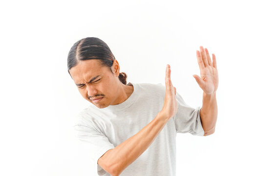 A man showing a defensive hand gesture with his eyes closed, expressing rejection, protest, or discomfort in a studio setting against white background.