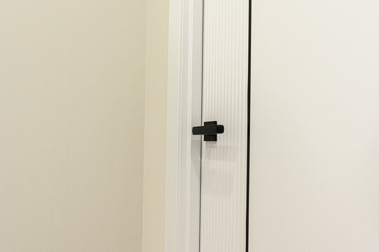 minimalist interior door in off‑white features vertical ribbed detailing and a sleek matte black lever handle; clean white trim contrasts with the pale beige wall