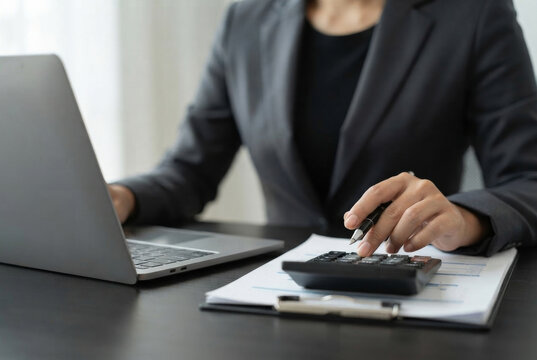 Businessman using calculator and laptop for financial accounting. Concept of tax calculation, business audit, budget planning, and cost analysis on office desk with paperwork graphs.