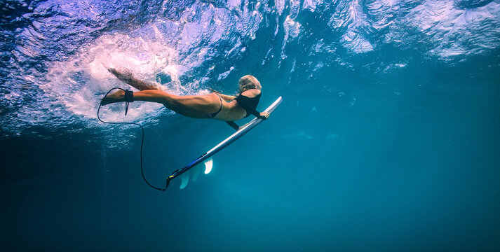 Underwater shot of female surfer diving with surfboard in clear