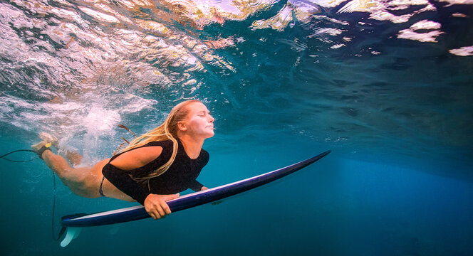 Serene Underwater Shot of Female Surfer Paddling Beneath Waves