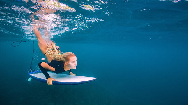 Underwater Shot Of Beautiful Blonde Female Surfer Paddling On Bo