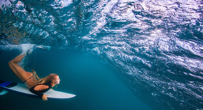 Underwater View Of Blonde Surfer Paddling On Board In Blue Ocean