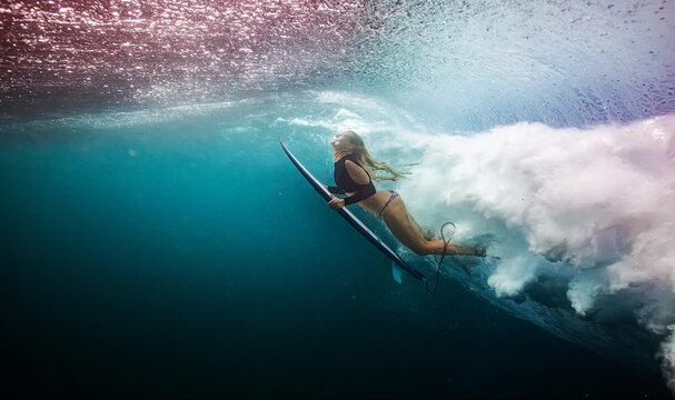 Blonde Female Surfer Floating On Surfboard Underwater During A W