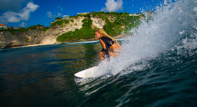 Female Surfer Riding a Wave with Spray and Coastal Cliffs Backgr