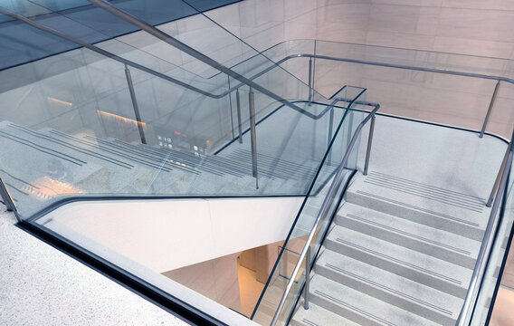 Modern stainless steel and glass staircase with safety handrails and geometric shadow patterns