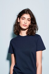 Fototapeta premium Young woman in a navy cotton t-shirt standing against a pale blue background for apparel mockup and lifestyle clothing brand display