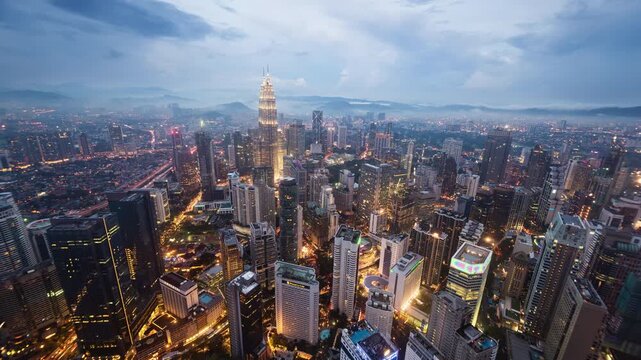 Asia, Malaysia, day to night transition time lapse of the Kuala Lumpur skyline and financial district at dusk, showing skyscrapers and the Petronas towers, high angle view 