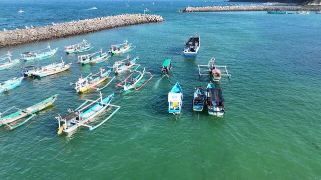 Top-down aerial footage of traditional blue wooden fishing boats neatly moored side-by-side along ropes in shallow.