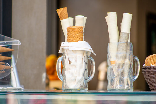 Waffle Ice Cream Cones and Paper Wrappers inside Large Glass Mugs on the Counter of Gelato Shop.