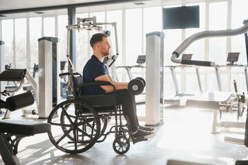 Obraz premium Man in wheelchair lifting dumbbells during rehabilitation in gym