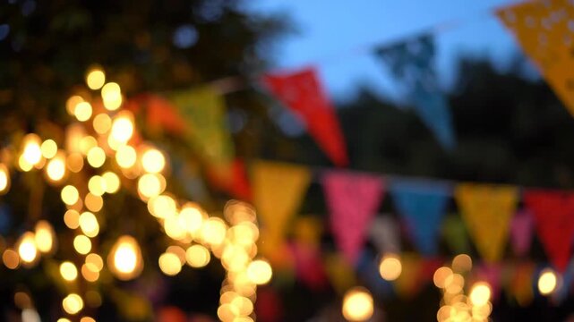 Bokeh lights and colorful flags create a festive atmosphere at an outdoor evening event.
