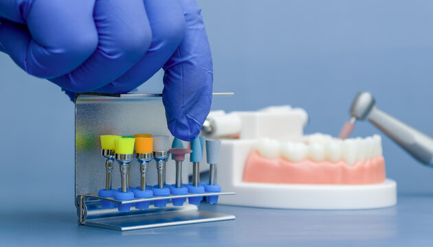 dentist hand in a blue glove picking a silicone polishing point from a metal bur block. Dental clinic concept.