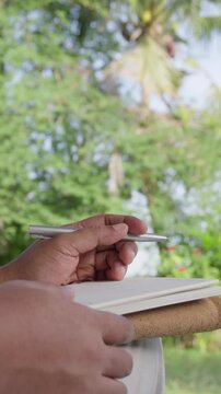 Business professional thinking before writing notebook while gently tapping finger on paper outdoors, representing creative thinking, strategic planning, problem solving, decision making, focused work