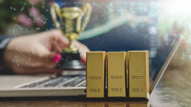 Digital gold trading and financial network concept. Gold bars on a laptop with a blurred woman holding a winner trophy and futuristic plexus overlay.