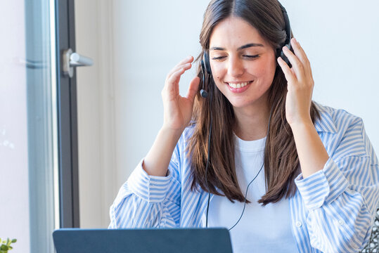 Smiling woman providing customer service on a headset while working remotely at a laptop, participating in a virtual call and online meeting in a bright home office.