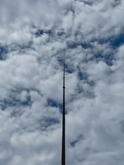 Obraz premium A towering lightning rod pierces a dramatic, cloudy sky streaked with deep blue. A minimalist, vertical shot from a low angle shows the contrast between the man-made structure and nature.