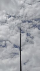 Obraz premium A towering lightning rod pierces a dramatic, cloudy sky streaked with deep blue. A minimalist, vertical shot from a low angle shows the contrast between the man-made structure and nature.
