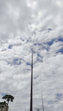 A towering lightning rod pierces a dramatic, cloudy sky streaked with deep blue. A minimalist, vertical shot from a low angle shows the contrast between the man-made structure and nature.