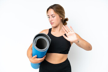 Naklejka premium Young caucasian woman going to yoga classes while holding a mat isolated on white background making stop gesture and disappointed