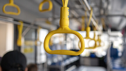 Yellow plastic hand straps hanging from a metal rail inside a public transit bus for passenger safety © Andik