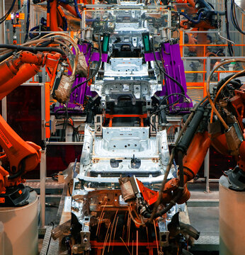 Automated robotic arms are welding at an automobile production plant.